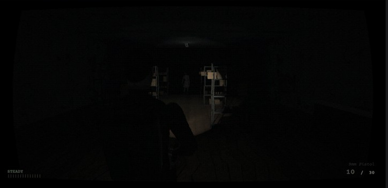 The same aisle almost black, a pale figure standing between the shelves at the far end